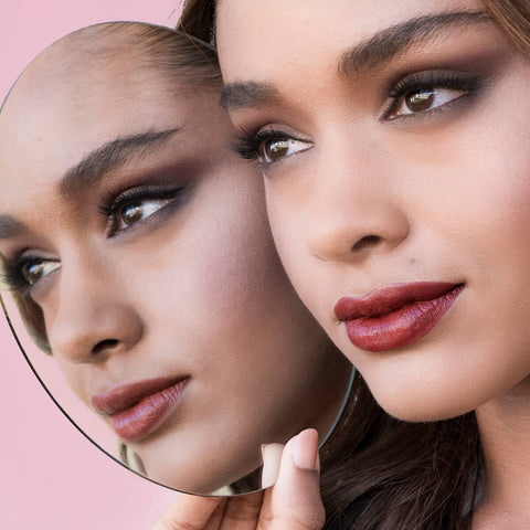Young woman with beautiful brown hair & skin tone, wearing bordeaux rouge lipstick. Reflected in a hand-held mirror.