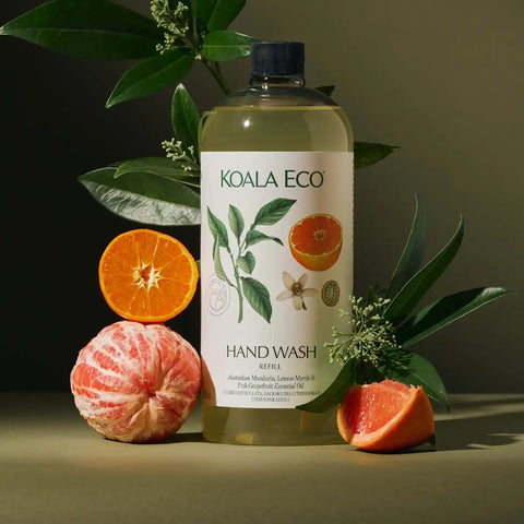 A bottle of hand wash refill with citrus and greenery props, photographed in a styled studio setup with a dark olive background.