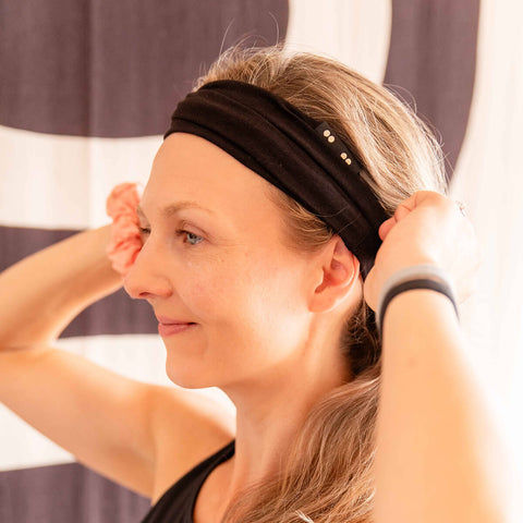 Woman with a black headband adjusting her hair against a blurred background