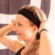 Woman with a black headband adjusting her hair against a blurred background