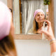 Woman applying a product to her face in front of a mirror.