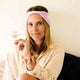 Woman wearing a light pink headband holding a small plant against a white background.