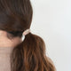 Person with a ponytail wearing a blond hair tie on a white background