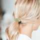 Close-up of blonde hair tied with a green hair tie against a blurred background