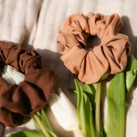 Two brown scrunchies on a piece of soft fabric with white tulips and leaves.