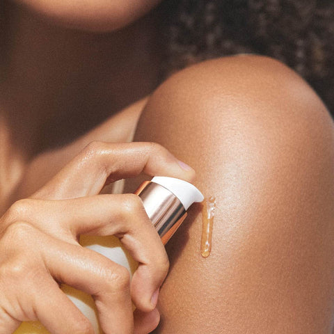Close-up of model pumping a small amount of body oil onto her shoulder. 