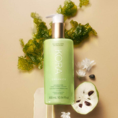 Kora Organics Nourishing Hand & Body Lotion product with green leaves and a halved fruit on a beige background.