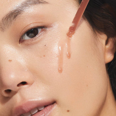 Close-up of a model using a dropper applicator with turmeric glow drops on her cheek.