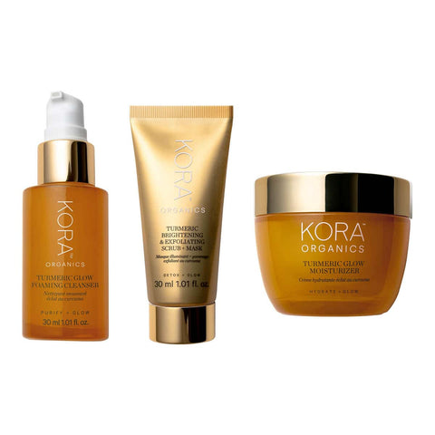 Kora Organics skincare products including cleanser, scrub-mask, and moisturiser on a white background. Amber & gold packaging.