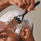 Person shaving their head with a razor and shaving cream on a neutral background