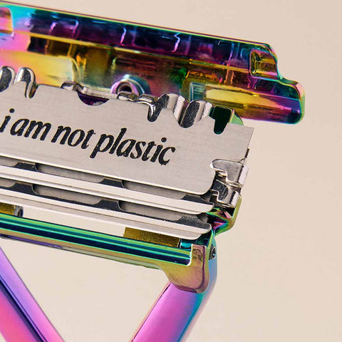 Multicolored safety razor with a blade that says 'I am not plastic' on a beige background