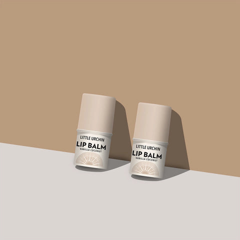 Two lip balm tubes standing upright on a light surface against a warm beige background.