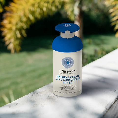 Little Urchin natural clear zinc sunscreen bottle on a stone ledge with greenery in the background.