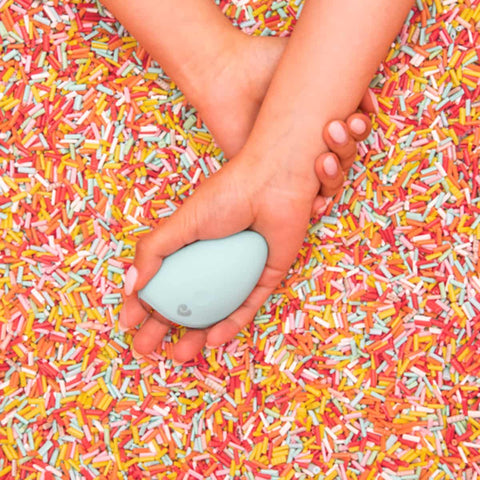 Hand holding a small blue personal massager on a background of colourful sprinkles.