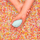 Hand holding a small blue personal massager on a background of colourful sprinkles.