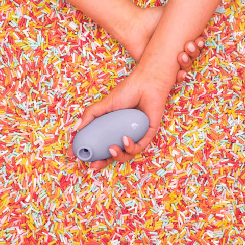 Hand holding a purple air suction stimulator on a colourful sprinkles background.