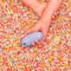 Hand holding a purple air suction stimulator on a colourful sprinkles background.