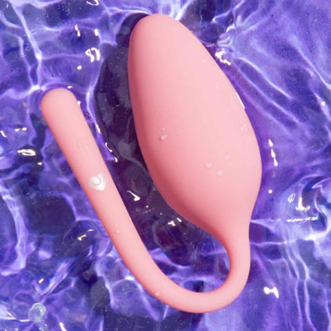Pink silicone vibrator in water on a purple background.