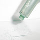 Green bottle releasing water droplets on a light grey background.
