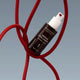 A bottle of MADARA Derma Collagen Peptide Serum with a white pump, set against a grey background with a red cable loop behind it.