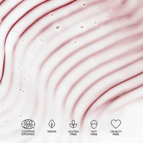 A close-up of a pale pink cosmetic cream or gel with wavy texture and small droplets, featuring five black icons along the bottom indicating COSMOS ORGANIC, VEGAN, GLUTEN FREE, NUT FREE, and CRUELTY FREE.