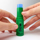 A green Dewy Hydra Caffeine Serum Stick with a blue cap, held between two hands against a light gray background.