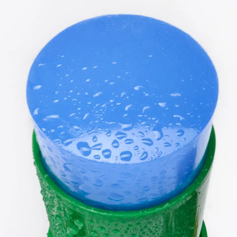 A close-up of a blue serum stick, covered in water droplets and sitting in a green container.