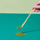 Wooden spoon with matcha powder on a turquoise and green background.