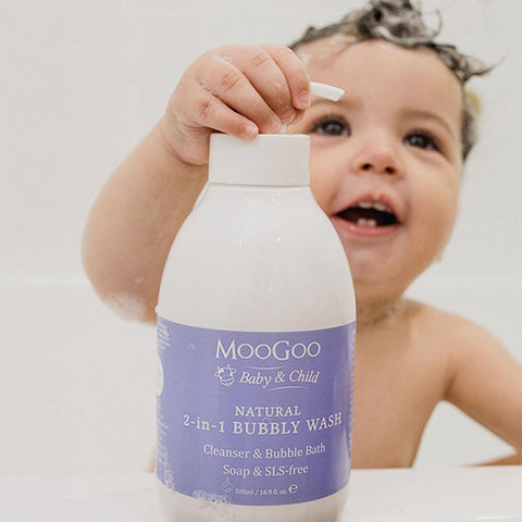 Child holding a bottle of Moogoo Baby & Child Natural Bubbly Wash with a plain background