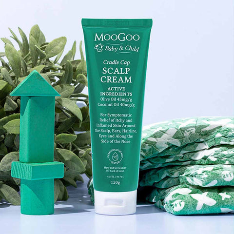 MooGoo Cradle Cap Scalp Cream with green packaging and styled with green wooden blocks and baby blanket.
