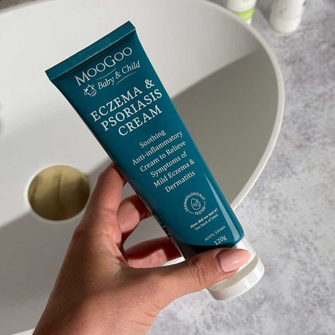 Hand holding a tube of Moogoo Baby & Child Eczema & Psoriasis Cream with a neutral background.