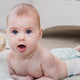 Baby lying on a bed wearing a nappy with a surprised expression