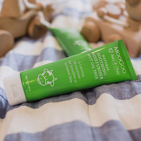 Green tube of Moogoo Baby & Child natural moisturiser on a striped fabric background