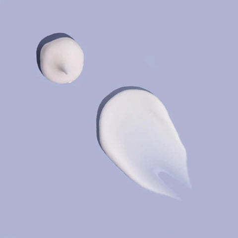 Two droplets of white cream on a light purple background.