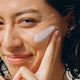 Woman applying a white cream to her face with a close-up view.