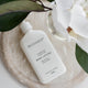 Mud Organics body lotion bottle on a stone surface with flowers and leaves.