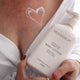 Woman holding a bottle of Mud Organics body lotion with a heart drawn on her chest with the lotion.
