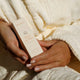 A person holding a cream-colored box of MUKTI Bioactive Renewal Day Serum, wrapped in a textured white robe.