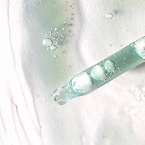 Close-up of dropper applicator filled with hyaluronic marine serum on a surface with more serum spread around.