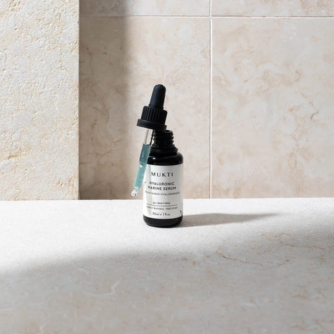 Mukti skincare serum bottle on a marble surface with a neutral background.
