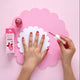 Child applying bright pink nail polish. Foam pink background & hand rest.