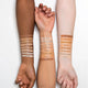 Three arms with different skin tones displaying a range of concealer swatches on the wrists.
