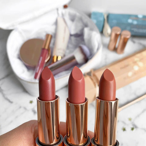Three lipsticks with rose gold cases on a blurred makeup set background.
