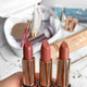 Three lipsticks with rose gold cases on a blurred makeup set background.