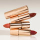 Three lipsticks with rose gold cases stacked on a light background.