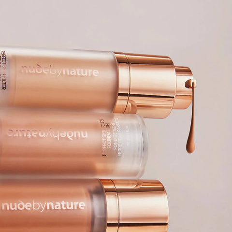 Three foundation bottles with rose gold caps and Nude by Nature branding on a light background.