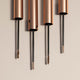 Four rose gold mascara tubes with black threads on a beige background.