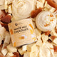 Collagen White Hot Chocolate mix surrounded by white chocolate pieces and a small cup of hot chocolate.