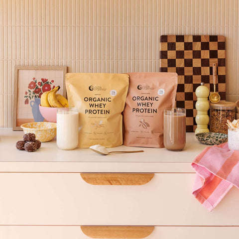 Two bags of Nutra Organics Organic Whey Protein range on a kitchen counter with glasses of protein shake.