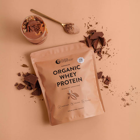Bag of Nutra Organics Organic Whey Protein - Chocolate 750g with chocolate pieces and a glass on a peach background.